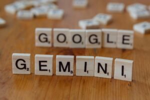 Scrabble tiles spelling out Google and Gemini on a wooden table, focusing on AI concepts.